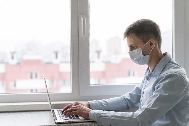 side view of a man with medical mask working on his laptop